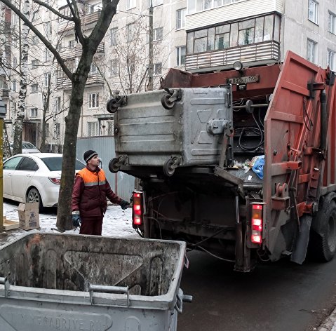 Сотрудник коммунальных служб выгружает мусор из контейнера в мусоровоз