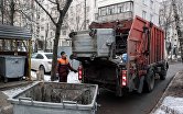 Сотрудник коммунальных служб выгружает мусор из контейнера в мусоровоз