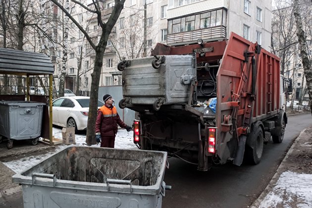 Сотрудник коммунальных служб выгружает мусор из контейнера в мусоровоз. ЖКХ